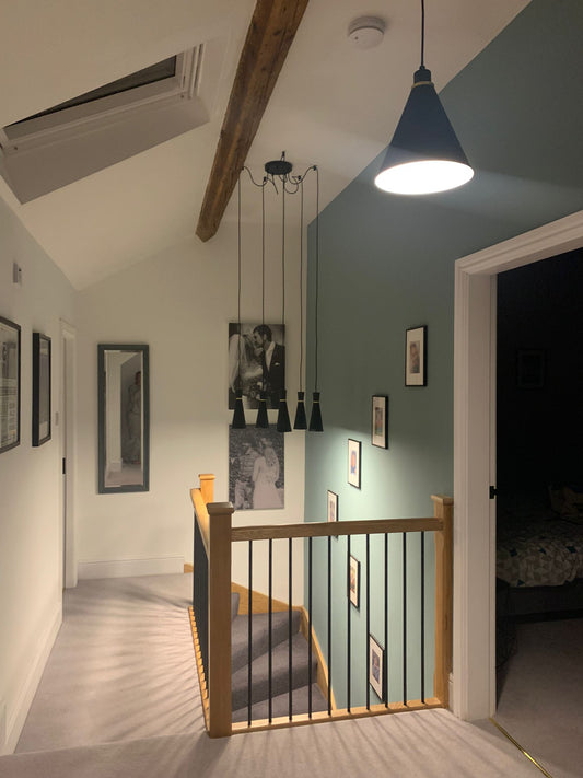 Modern interior hallway with wooden staircase, pendant lights, and framed pictures on the wall.