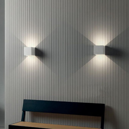 Two wall-mounted lights on a textured wall with a bench in the foreground.
