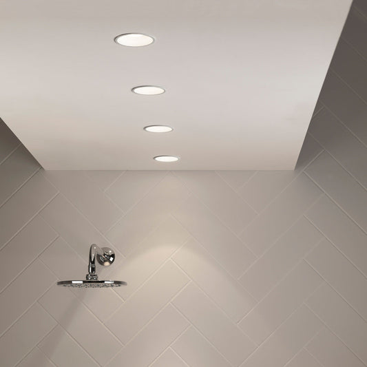 Shower head mounted on a tiled wall with recessed ceiling lights.