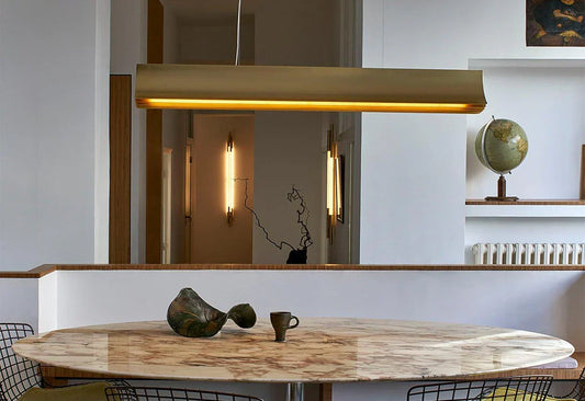 DCW Editions Respiro gold linear pendant over oval marble dining table with Org vertical wall lights in the background