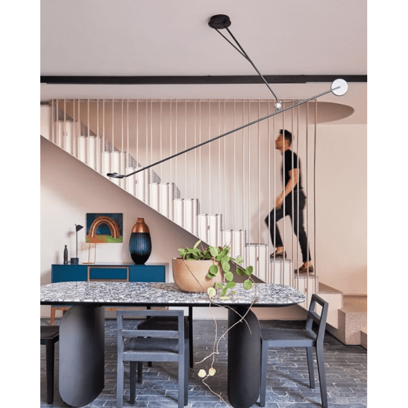 DWC Editions Aaro ceiling light over oval dining table with man going up stairs
