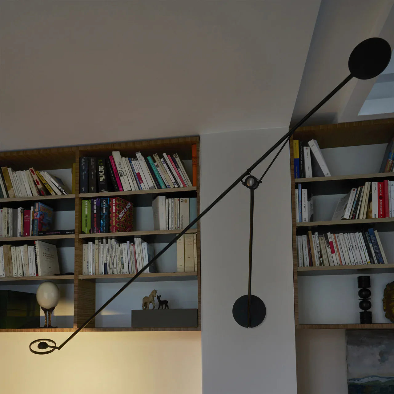 DWC Editions Aaro wall light on a slim wall in a room with many books