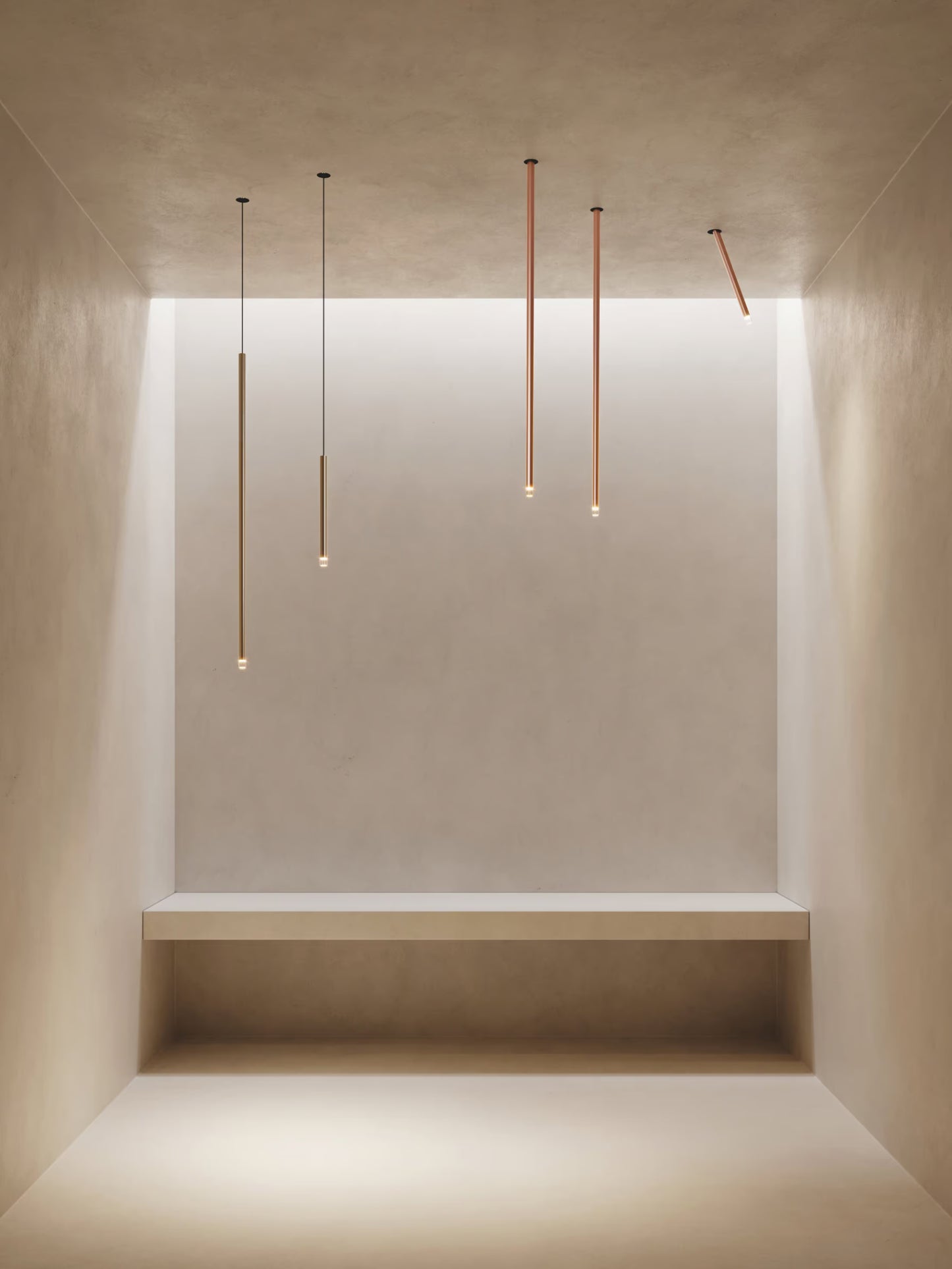 Lodes A-Tube Nano pendants and swing ceiling lights in terra finish illuminated in minimalist plaster room with single bench