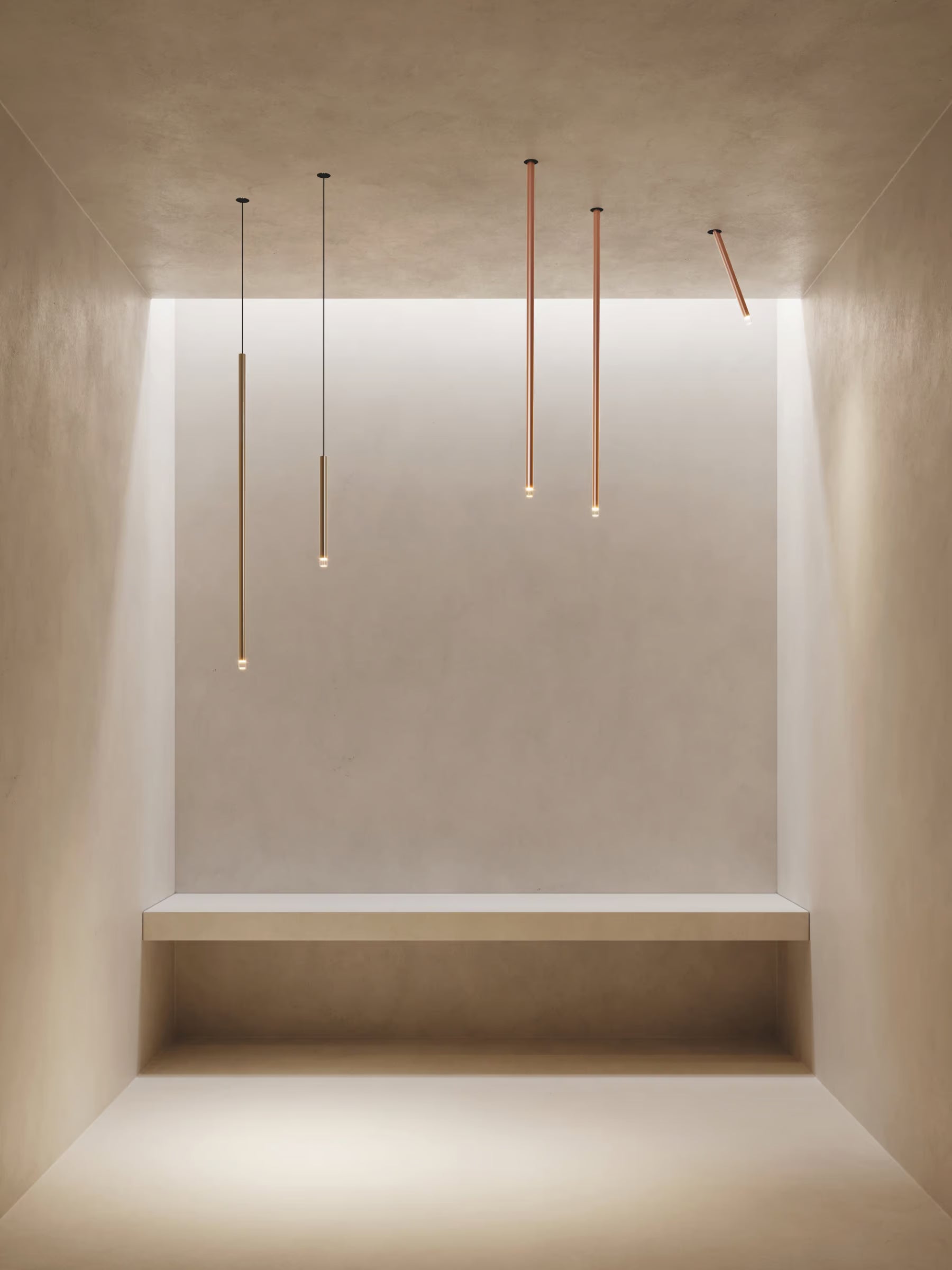Lodes A-Tube Nano pendants and swing ceiling lights in terra finish illuminated in minimalist plaster room with single bench