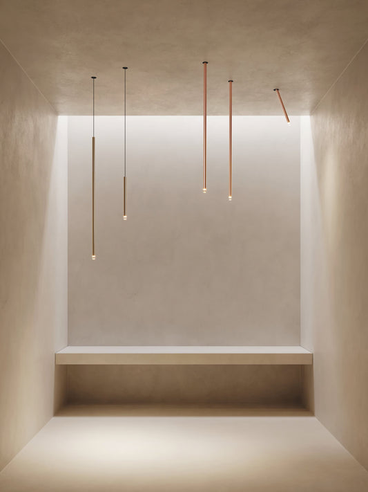 Lodes A-Tube Nano pendants and swing ceiling lights in terra finish illuminated in minimalist plaster room with single bench
