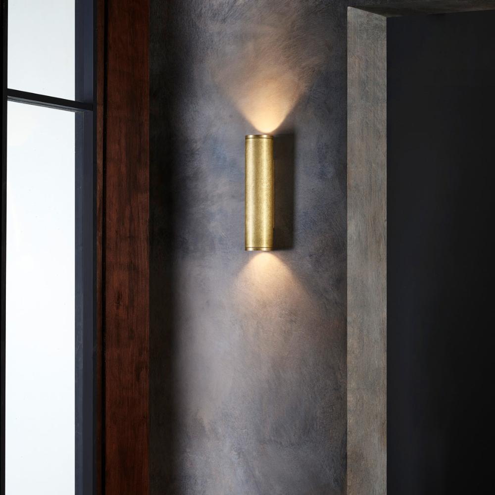 Gold wall sconce on a textured wall with a window in the background