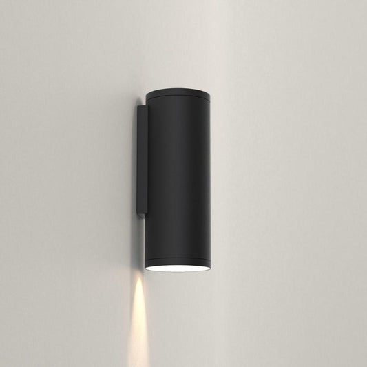 Black cylindrical wall light fixture on a gray wall