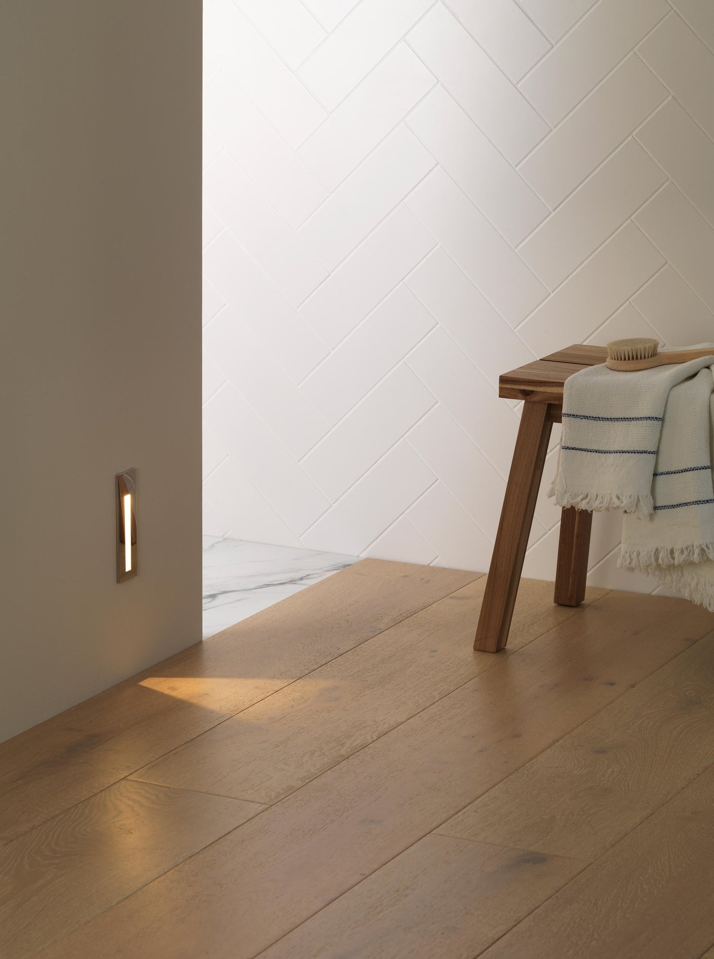Wooden floor with a wall-mounted light fixture and a wooden bench with a towel draped over it.
