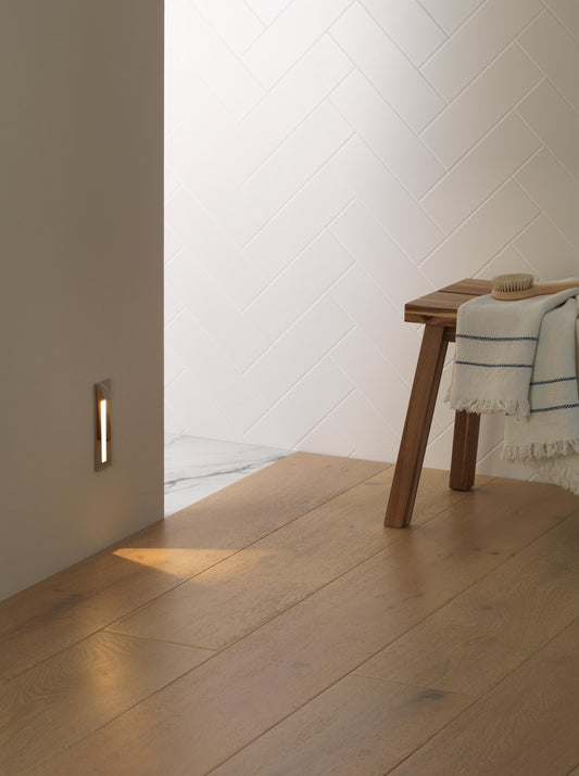 Wooden floor with a wall-mounted light fixture and a wooden bench with a towel draped over it.