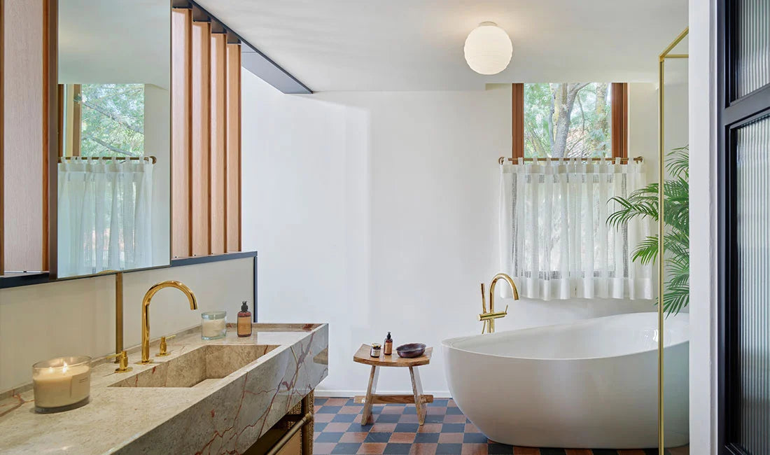 White globe ceiling light over bathtub in large bathroom with check floor and gold taps.