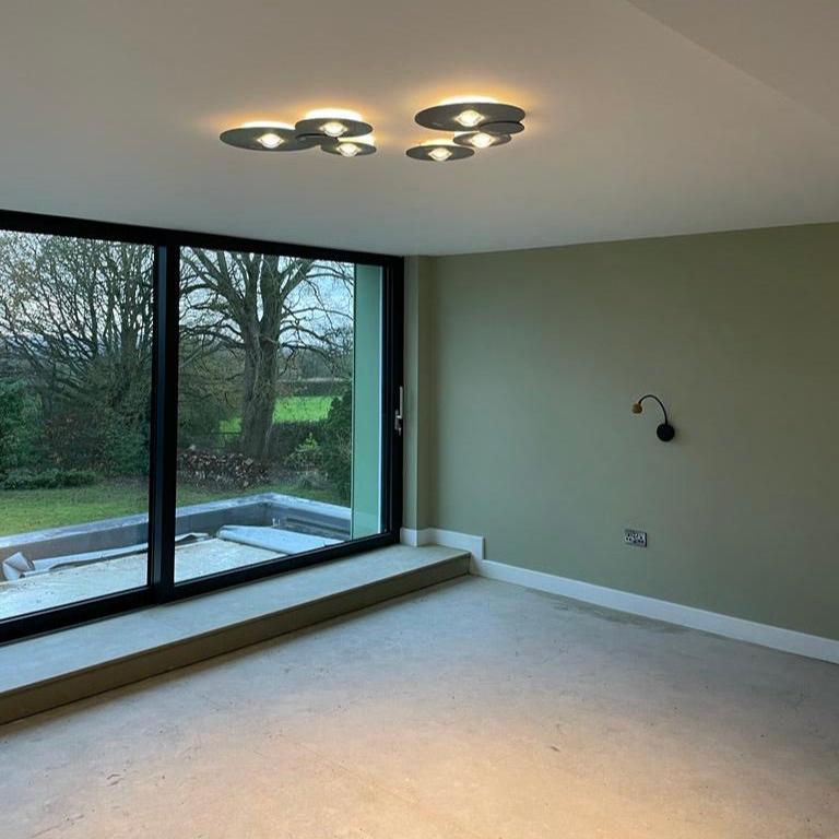 Modern bedroom with large windows, neutral walls, and ceiling lights.