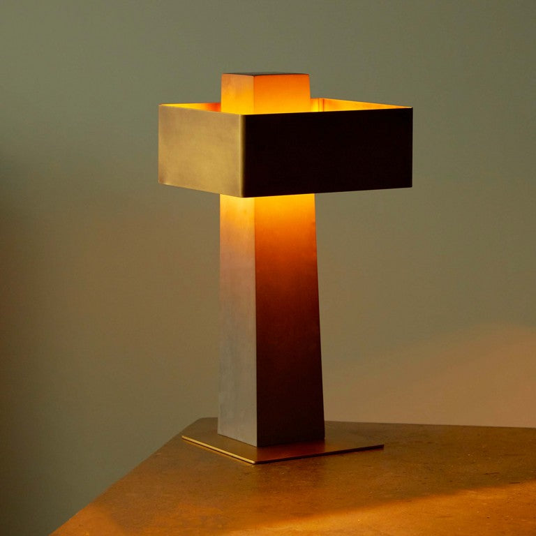 DCW Editions Iota table lamp in brass and bronze lit with warm light on edge of table