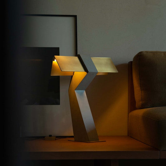 DCW Editions Iota table lamp in brass and bronze warmly lit by sofa