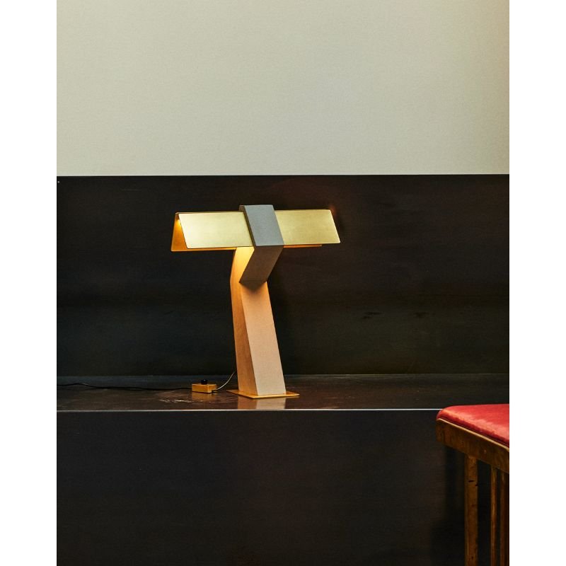 DCW Editions Iota table lamp in brass and bronze lit on dark table with red stool