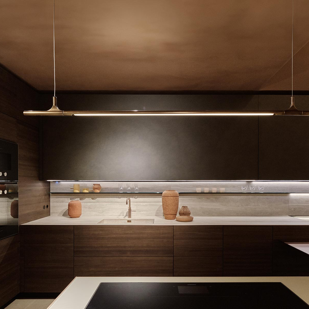 Modern kitchen with dark cabinets, a light, a sink, and decorative vases.