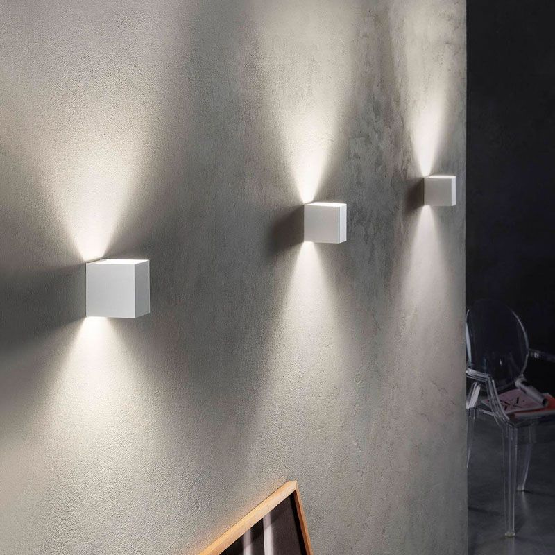 Three square wall lights on a textured wall with a dark room in the background.