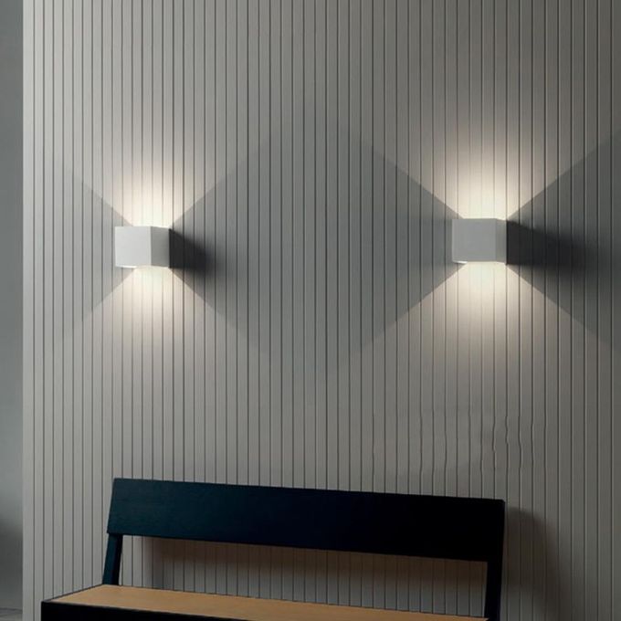 Two wall-mounted lights on a textured wall with a bench in the foreground.