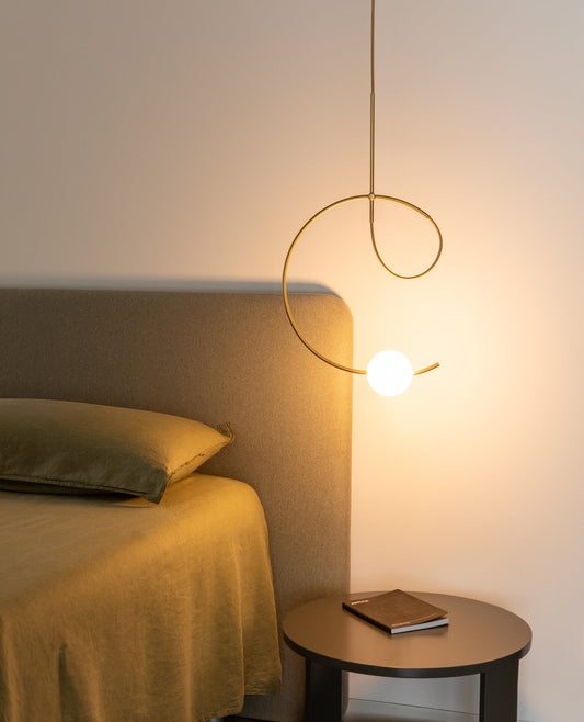 Estiluz Loop Pendant in gold finish with illuminated white sphere hanging over a round bedside table
