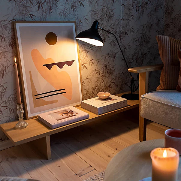 DCW Editions Mantis table lamp on low side table with books, art and a candle