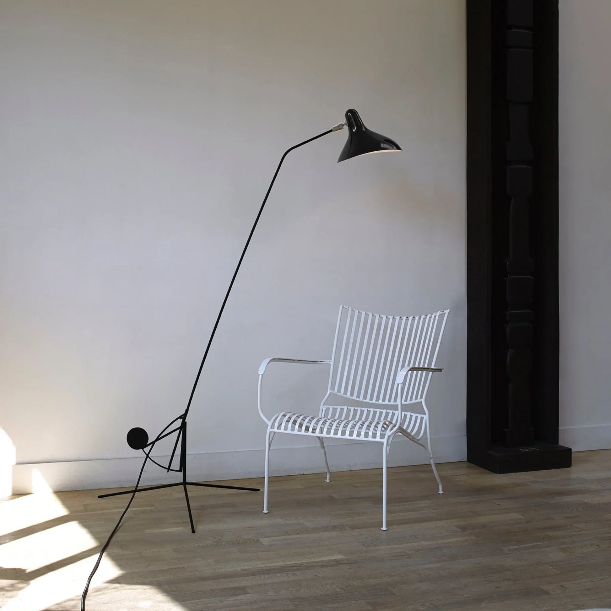 DCW Editions Mantis floor lamp BS1 next to white metal chair in white room with a black pillar