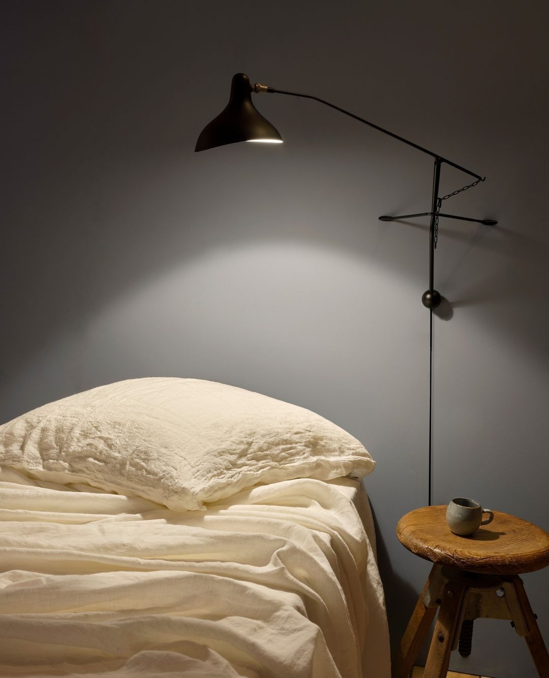 DCW Editions Mantis plug-in wall light BS2 above bed with cream linen and wooden side table