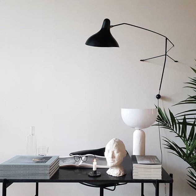 DCW Editions Mantis plug-in wall light BS2 above desk with books, a bust, table lamp and a candle