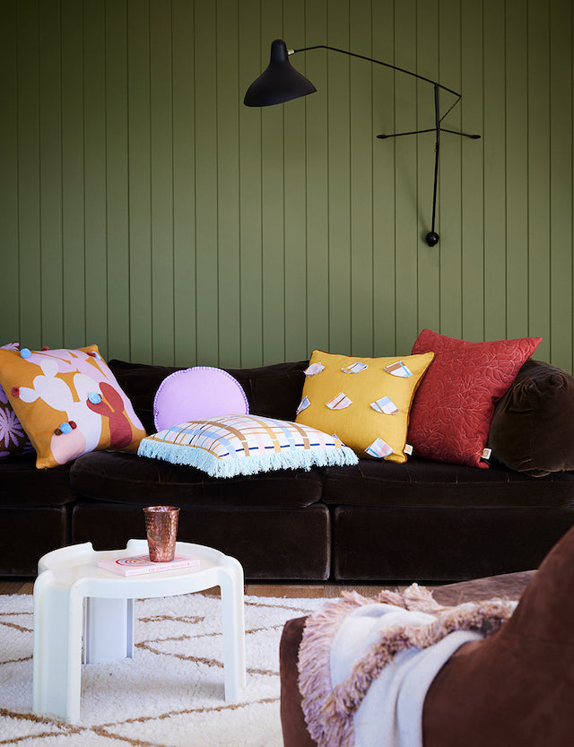 DCW Editions Mantis plug-in wall light BS2 on green panelled wall above dark velvet sofa with colourful cushions
