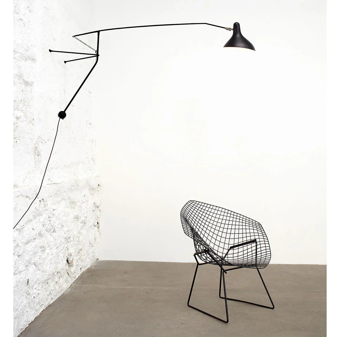 DCW Editions Mantis plug-in wall light BS2 on stone wall with black chair