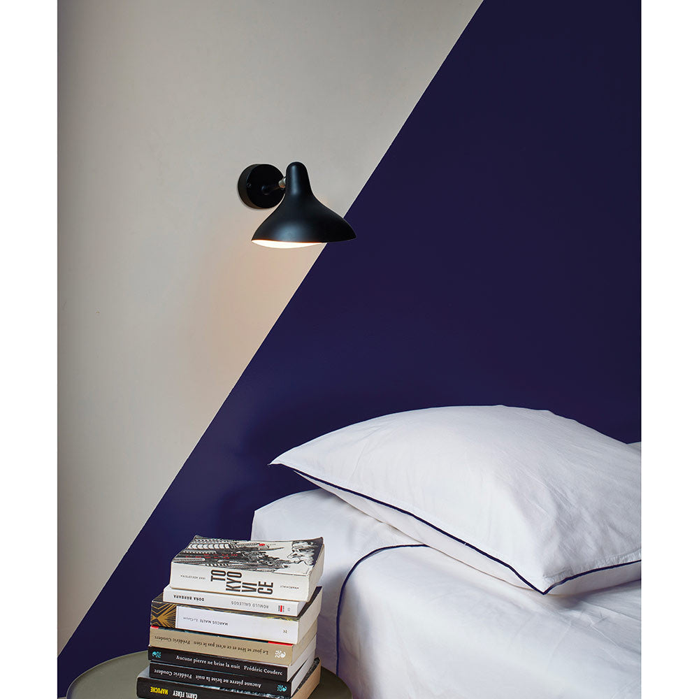 DCW Editions Mantis wall light mini BS5 on white and blue wall next to a bed with stack of books nearby
