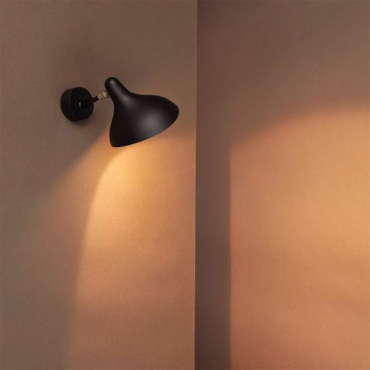 DCW Editions Mantis wall light mini casting a warm glow on a burnt orange wall