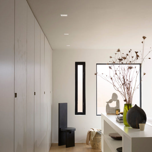 Modern interior with white walls, a shelf with decorative items, and a mirror.
