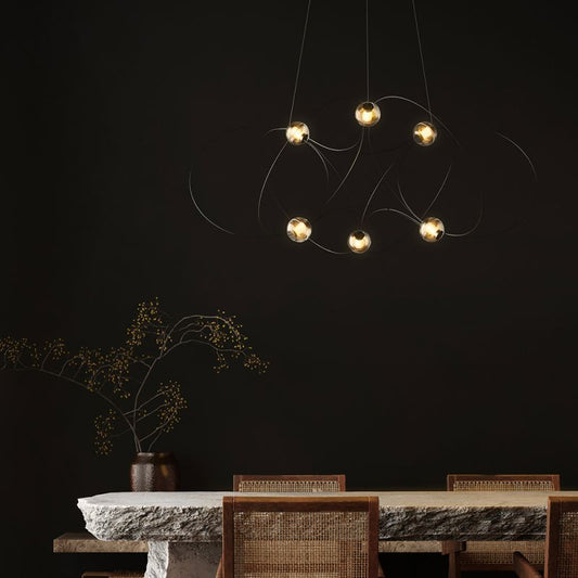 DCW Editions Munari pendant with 6 acrylic spheres and black curved rods warmly lit over stone table in room with dark wall