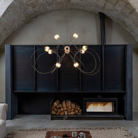 DCW Editions Munari pendant with 10 illuminated acrylic spheres and gold curved rods in lounge low furniture and wooden ceiling with modern fireplace in large, modern inglenook 