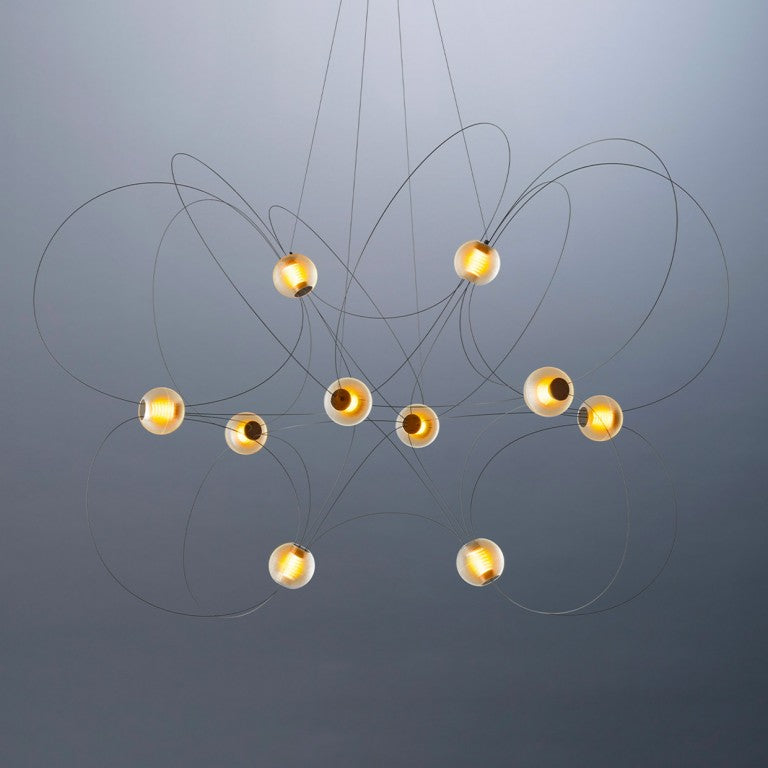 DCW Editions Munari pendant with gold, curved rods and 10 acrylic spheres with warm light on blue background