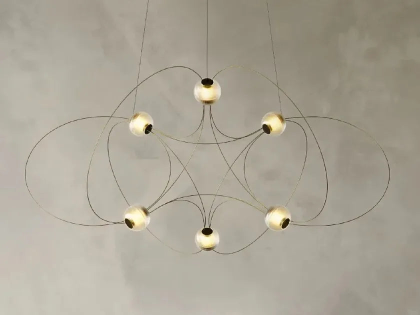 DCW Editions Munari pendant with 6 acrylic spheres and gold curved rods warmly lit on beige background