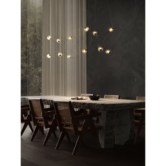 DCW Editions Munari pendants with acrylic spheres and black curved rods warmly lit by window over stone dining table with wooden chairs