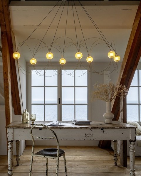 DCW Editions Munari pendant with 8 illuminated acrylic spheres and curved rods over rustic desk with chair in attic overlooking the sea