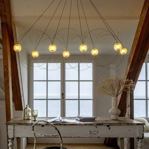 DCW Editions Munari pendant with 8 illuminated acrylic spheres and curved rods over rustic desk with chair 