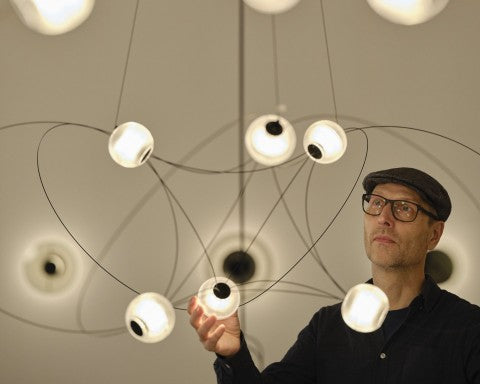 DCW Editions Munari pendant with designer gazing at the light and holding one of the spheres