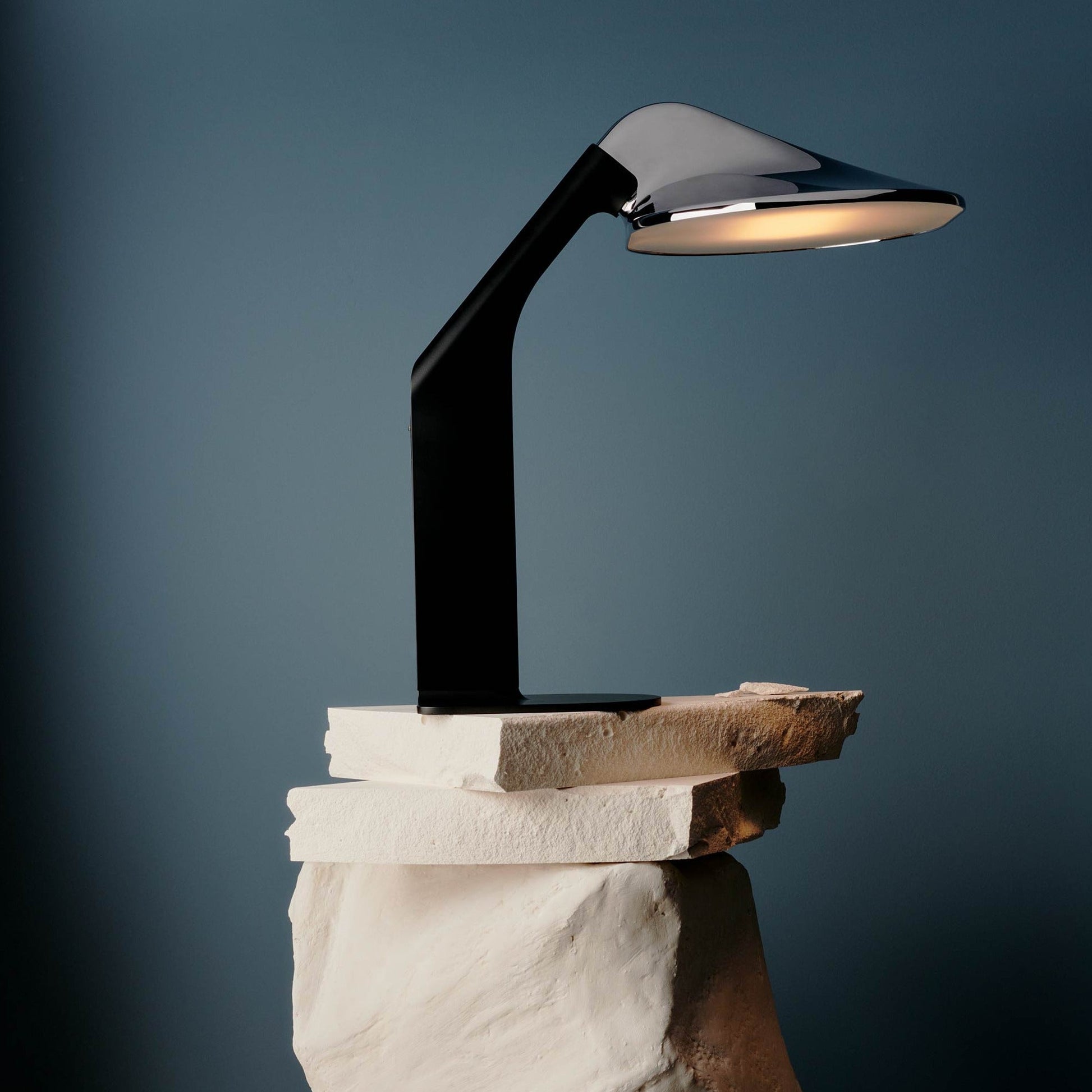 DCW Editions Niwaki black and chrome desk light on white, stacked stones with blue background