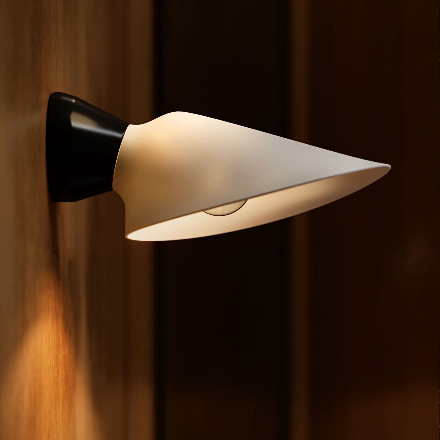 DCW Editions Plume wall light with white shade and black base on wooden wall, softly lit