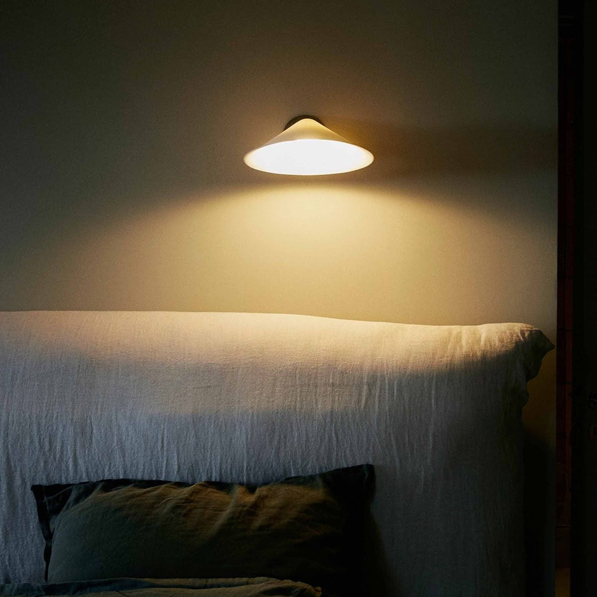 DCW Editions Plume wall light with white shade over fabric headboard