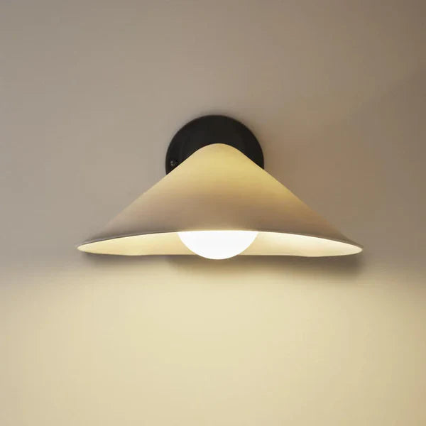 DCW Editions Plume wall light porcelain shade with black hardware, illuminated on beige wall