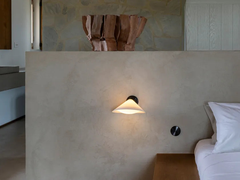 DCW Editions Plume Wall Light on a low plaster wall next to a bed on a wooden platform