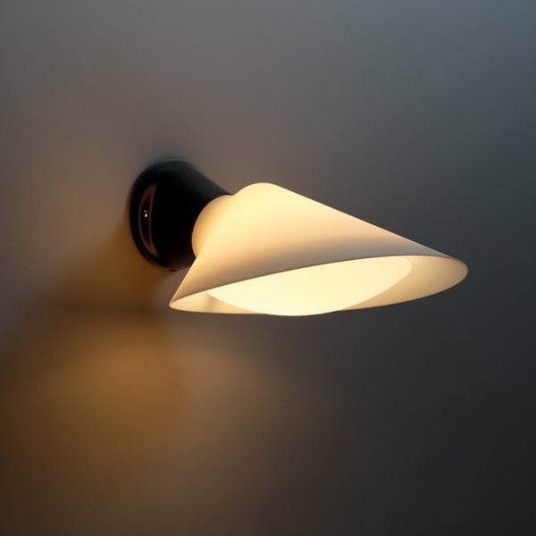 DCW Editions Plume wall light, warmly illuminated, with a bottom diffuser on a grey wall