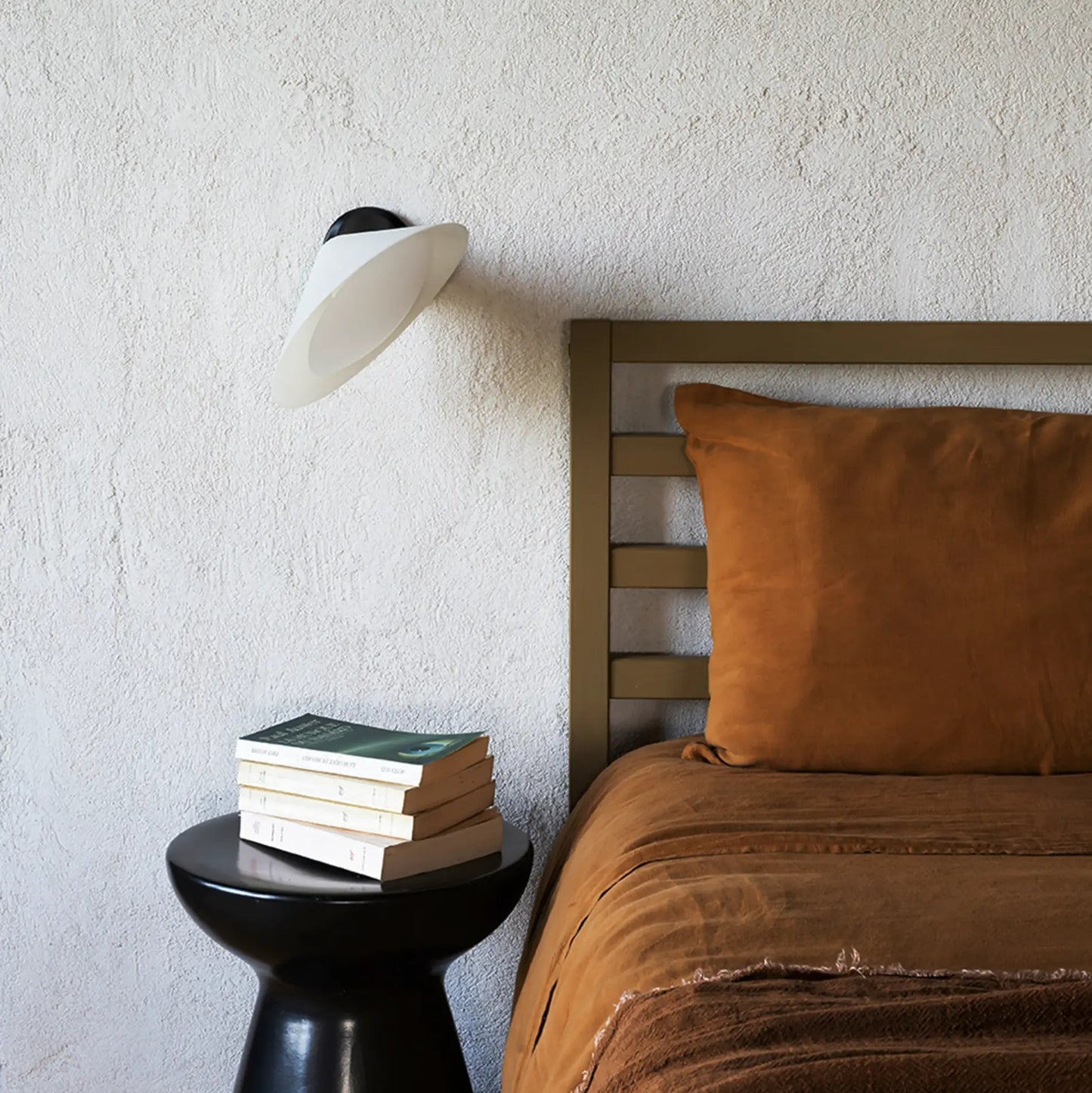 DCW Editions Plume wall light angled towards a bed with burnt orange linen bedding