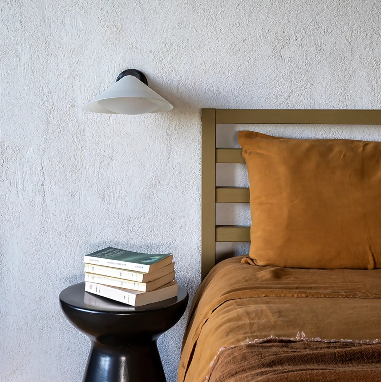 DCW Editions Plume wall light next to a bed with burnt orange linen bedding