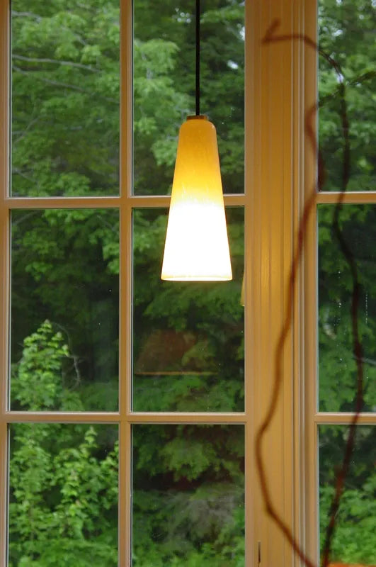 Slim glass pendant hanging over a sink in front of a window with greenery outside