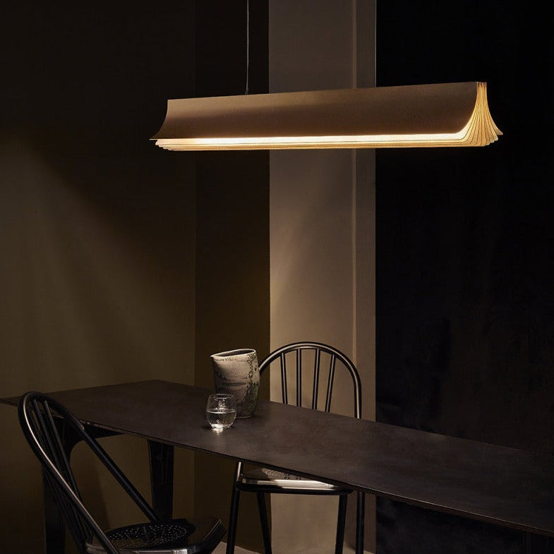 DCW Editions Respiro gold linear pendant over dark, narrow table with a glass of water and wonky vase