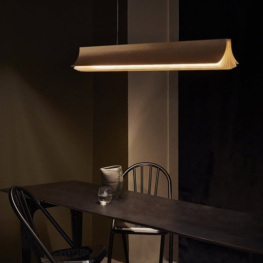 DCW Editions Respiro gold linear pendant over dark, narrow table with a glass of water and wonky vase